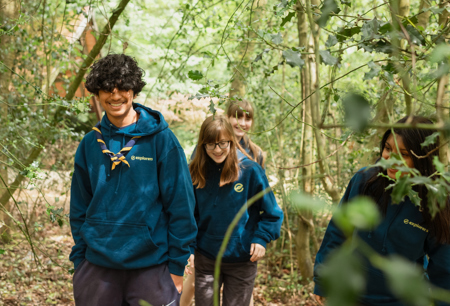 A group of Explorers smile while walking through a wooded area.