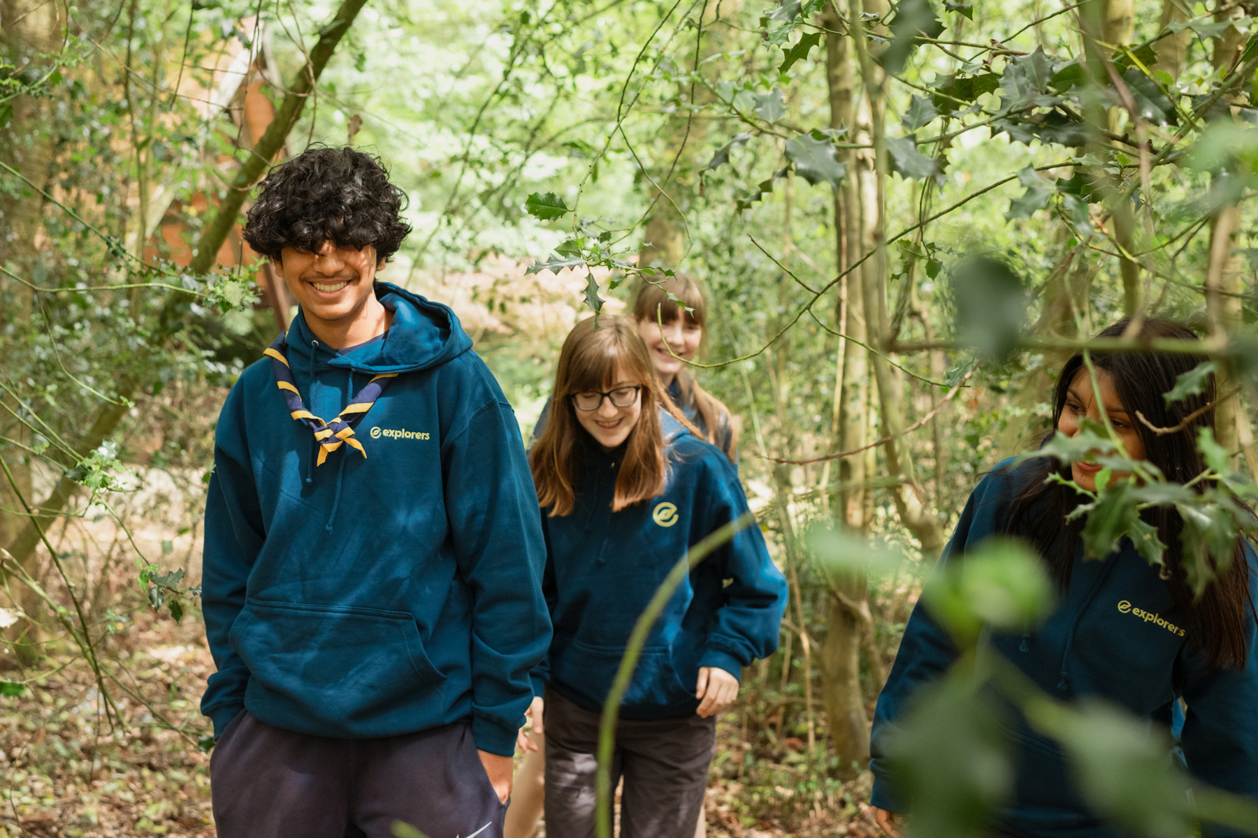 A group of Explorers smile while walking through a wooded area.