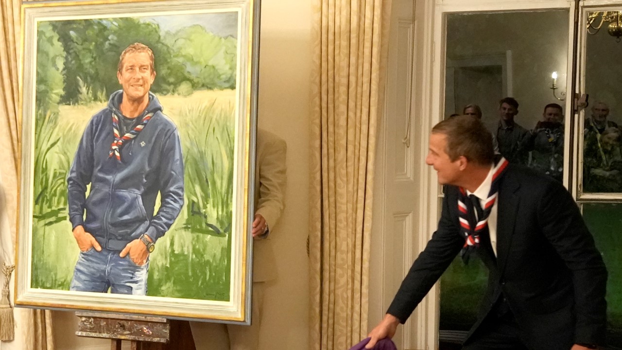 Bear Grylls unveils a portrait of himself in a large golden frame.