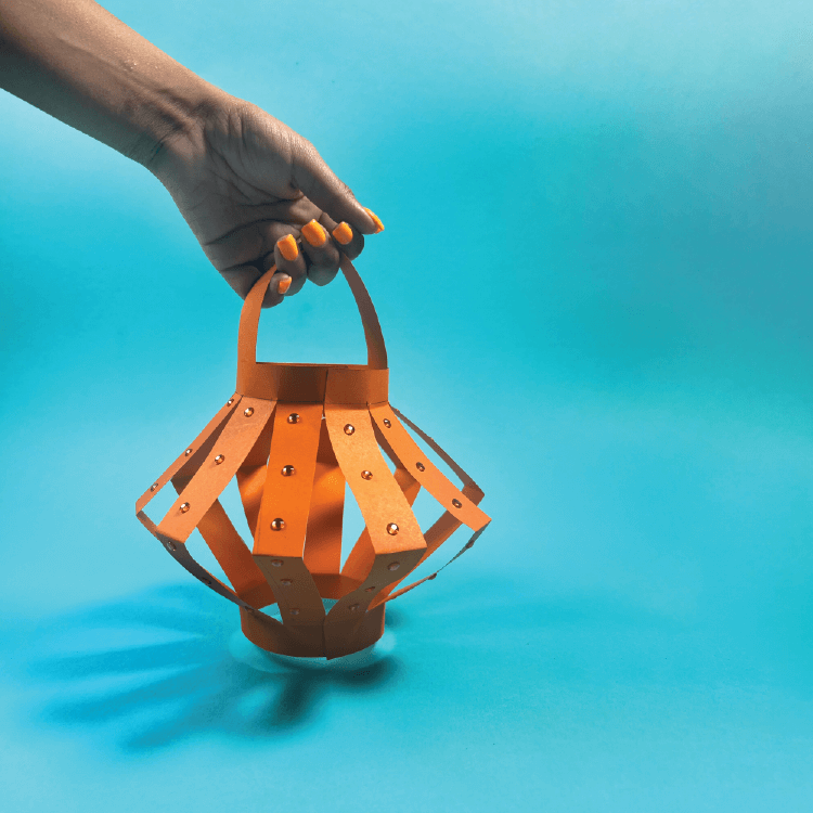 A hand holding an orange lantern made from paper cut into strips.