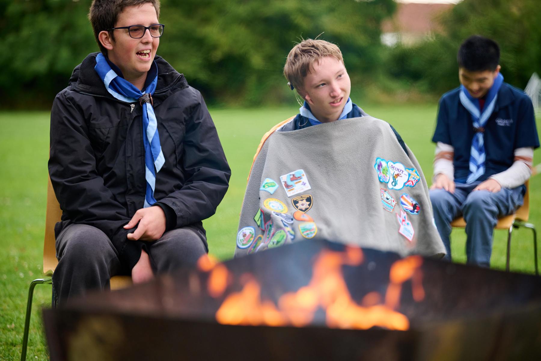 Two young people sit around a campfire.