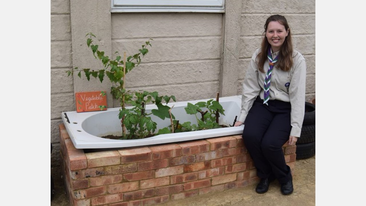 A young person in a Network uniform sitting by a bathtub filled with plants