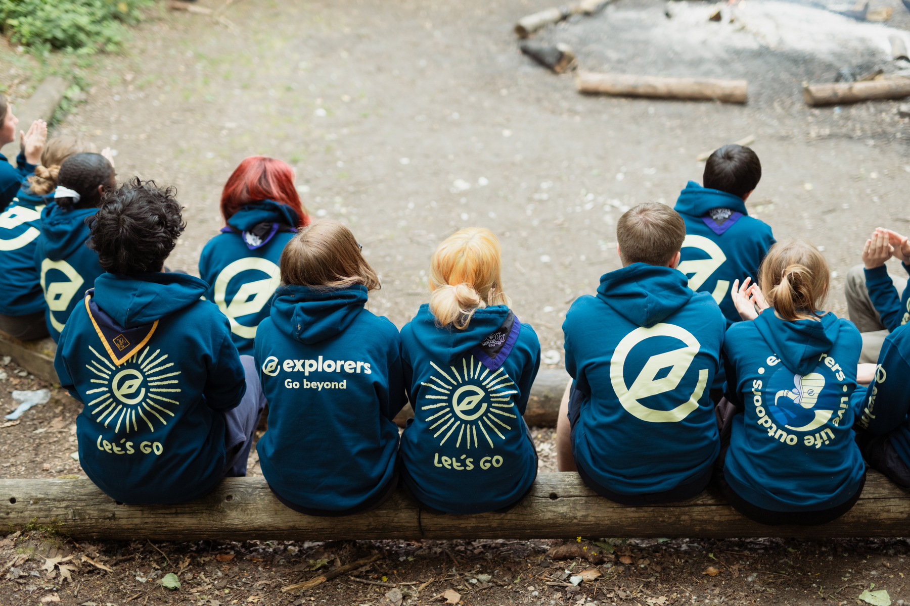 A group of Explorers sit on a log with their back to the camera.