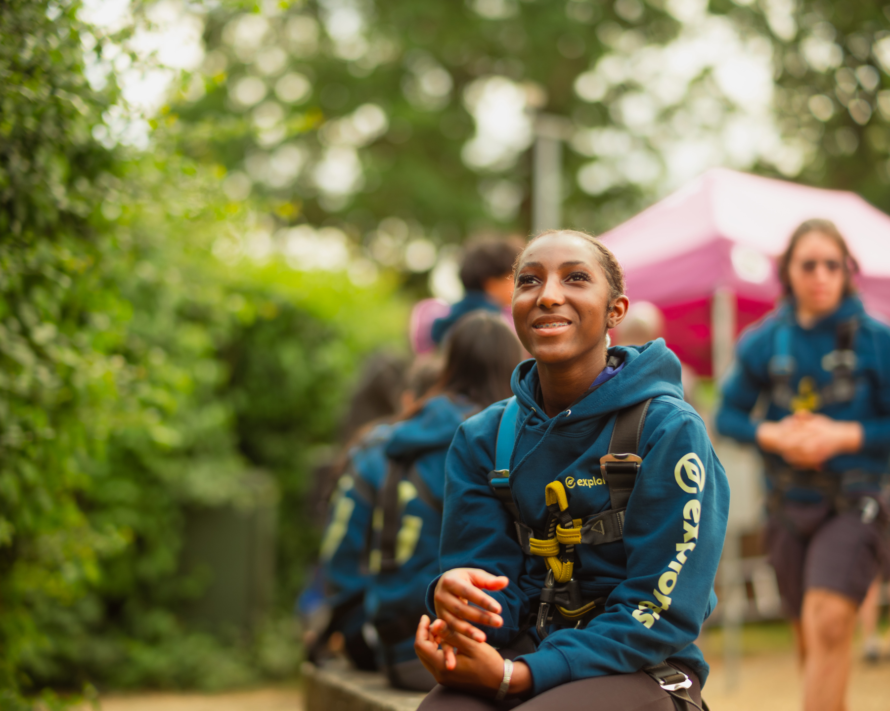 An Explorer wearing a hoodie and activity harness smiles while looking upwards