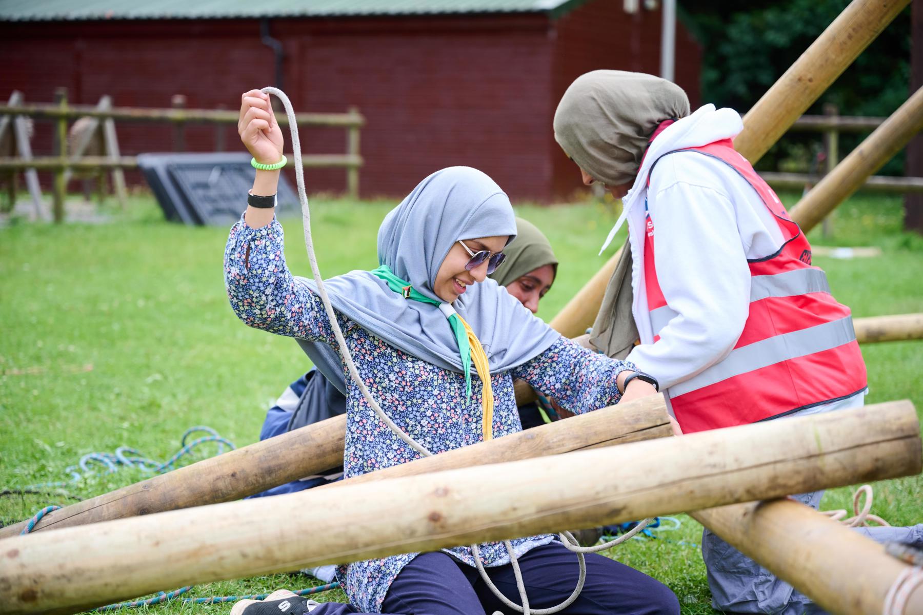 Three volunteers wearing hijabs pioneering with logs and rope outside.