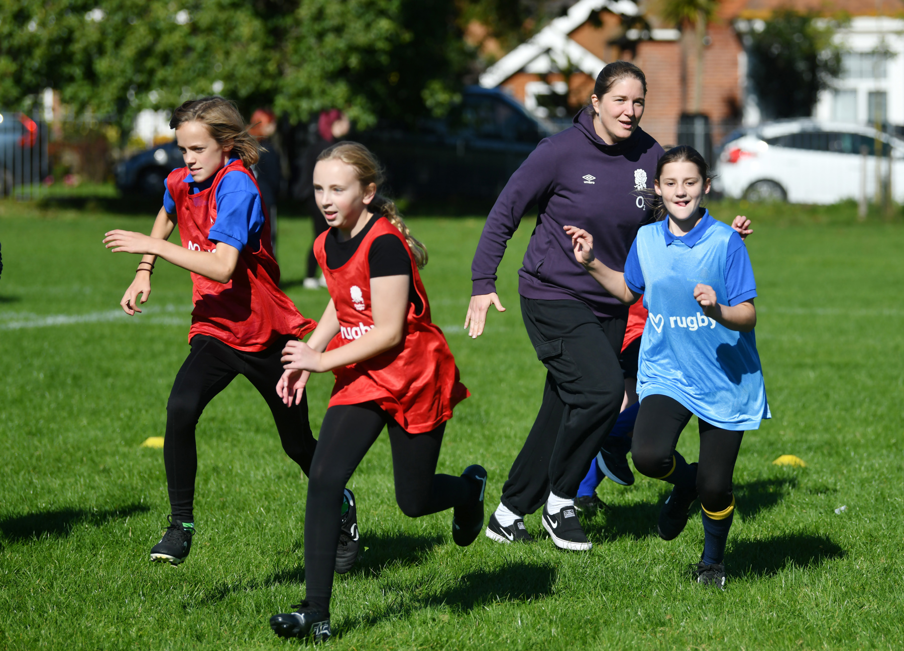 The image shows three Scouts running on a grass playing field. Two of the Scouts have red bibs on and are to the left of the image, and one to the right is wearing a blue bib.