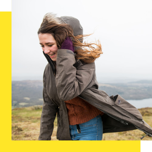A young person wearing a coat walks outside in the wind.