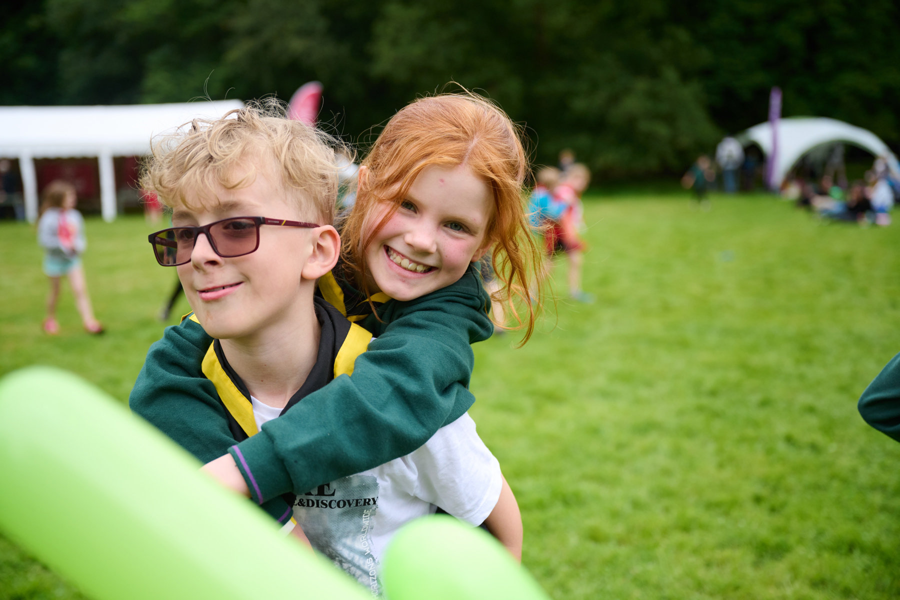 One young person puts their arms around the other while they both smile