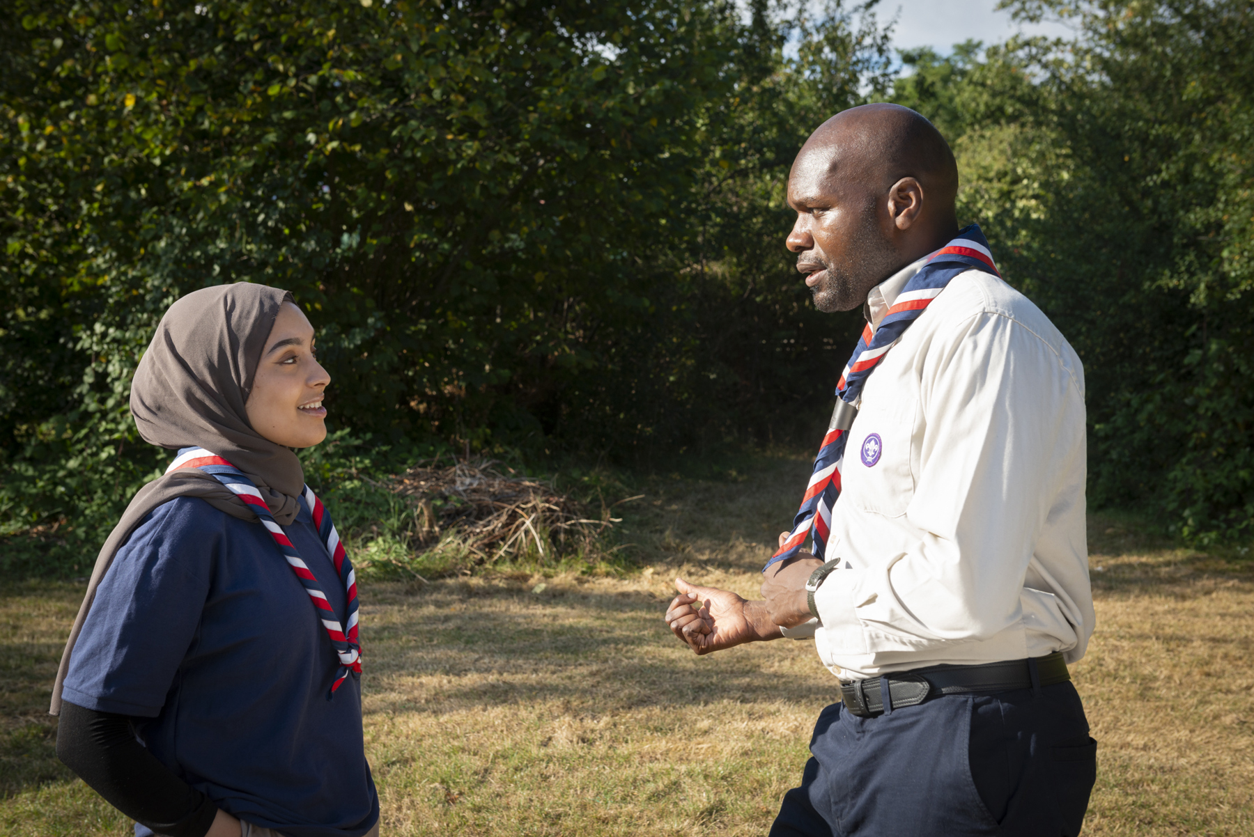 Image shows Dwayne Fields in necker and uniform talking to a female volunteer