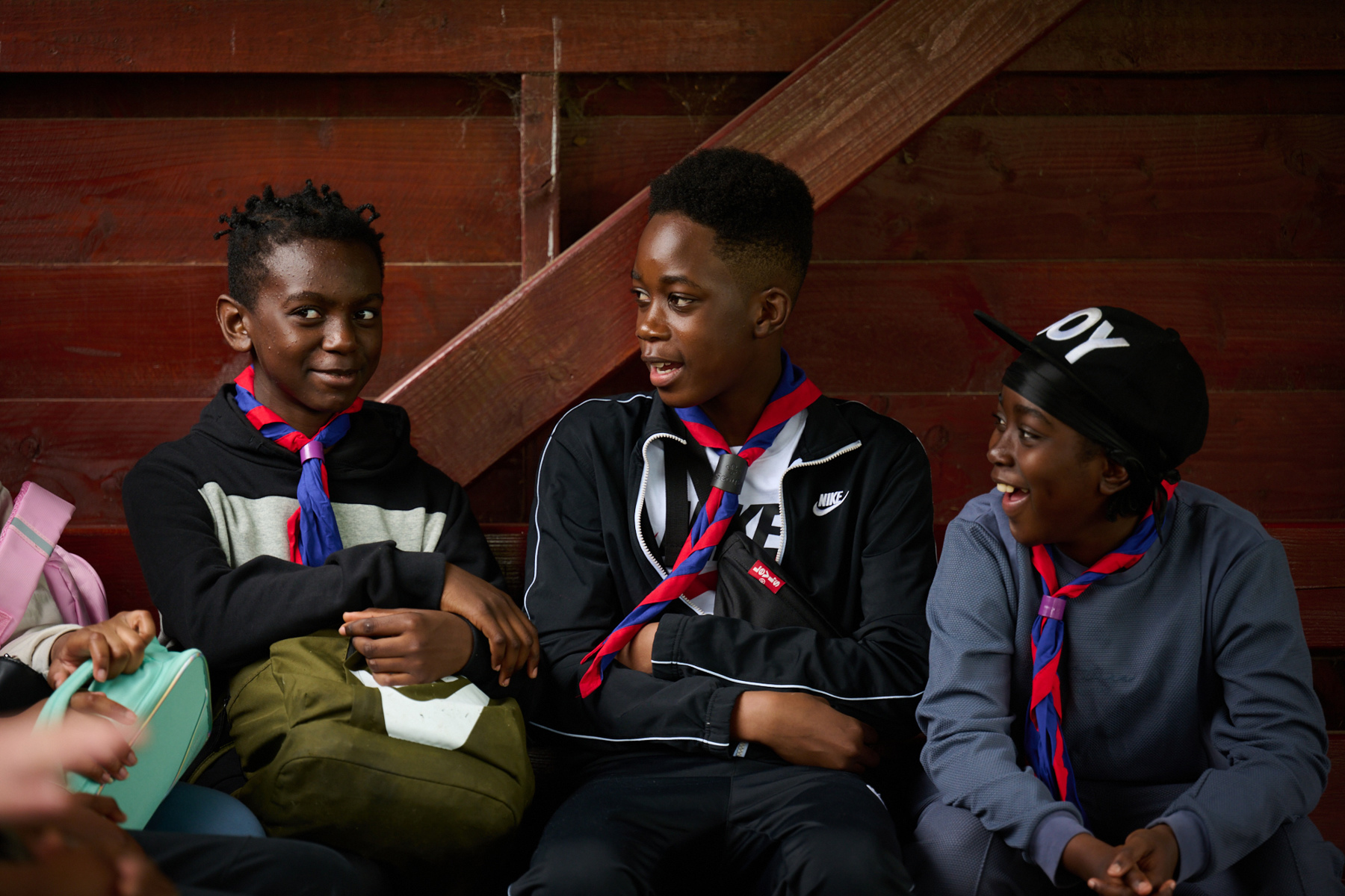 Group of three Scouts sat together indoors wearing blue and red scarves 