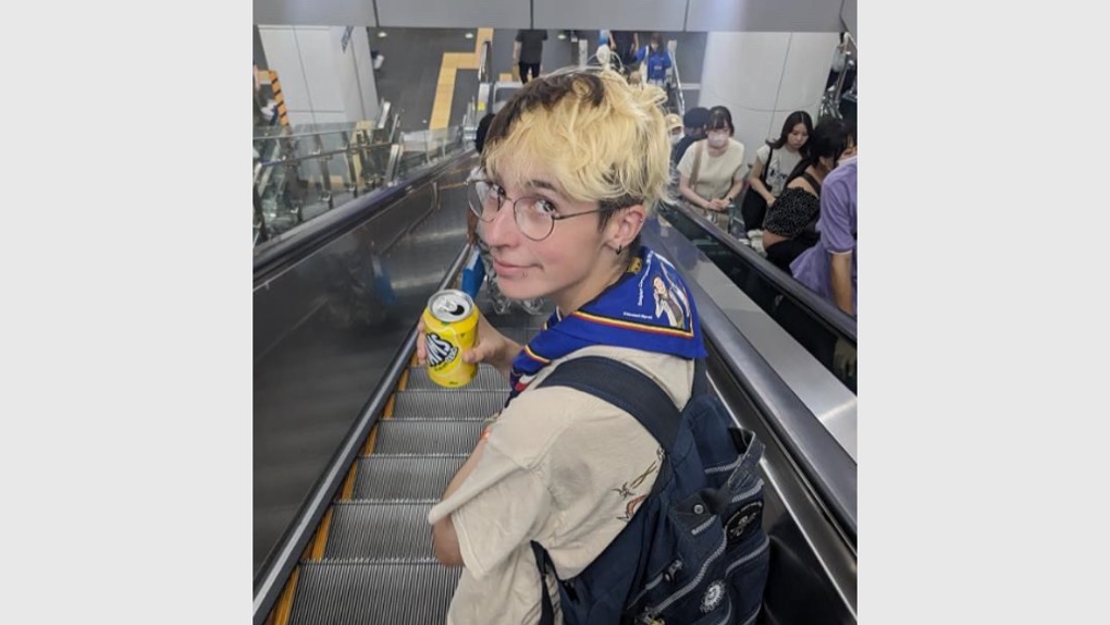 Volunteer Corry is wearing Scout uniform standing on an escalator and turning around to look at the camera.