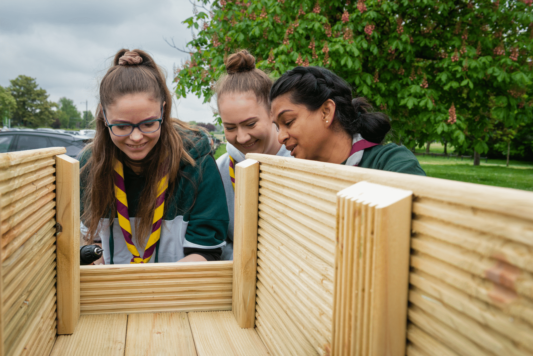 Three young volunteers building a planter together outside