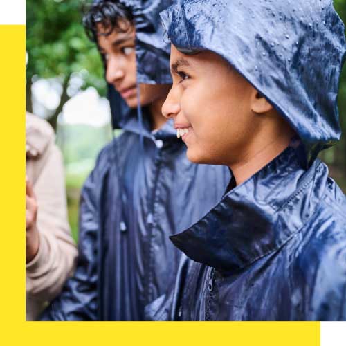 Two young people wearing raincoats smile while looking to the side. 