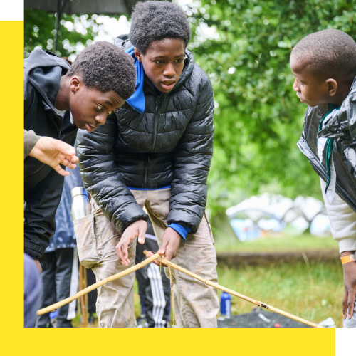Three young people concentrate while doing an outdoor activity with sticks.
