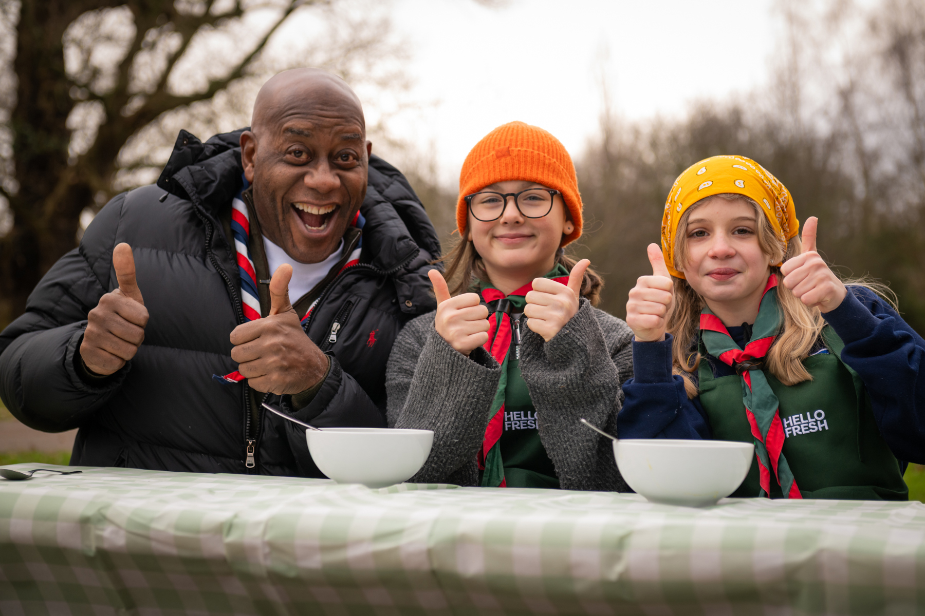 Ainsley Harriott and two Scouts smile while giving a thumbs up to the camera.