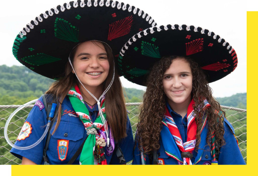 Two young people smile at the camera while wearing traditional hats
