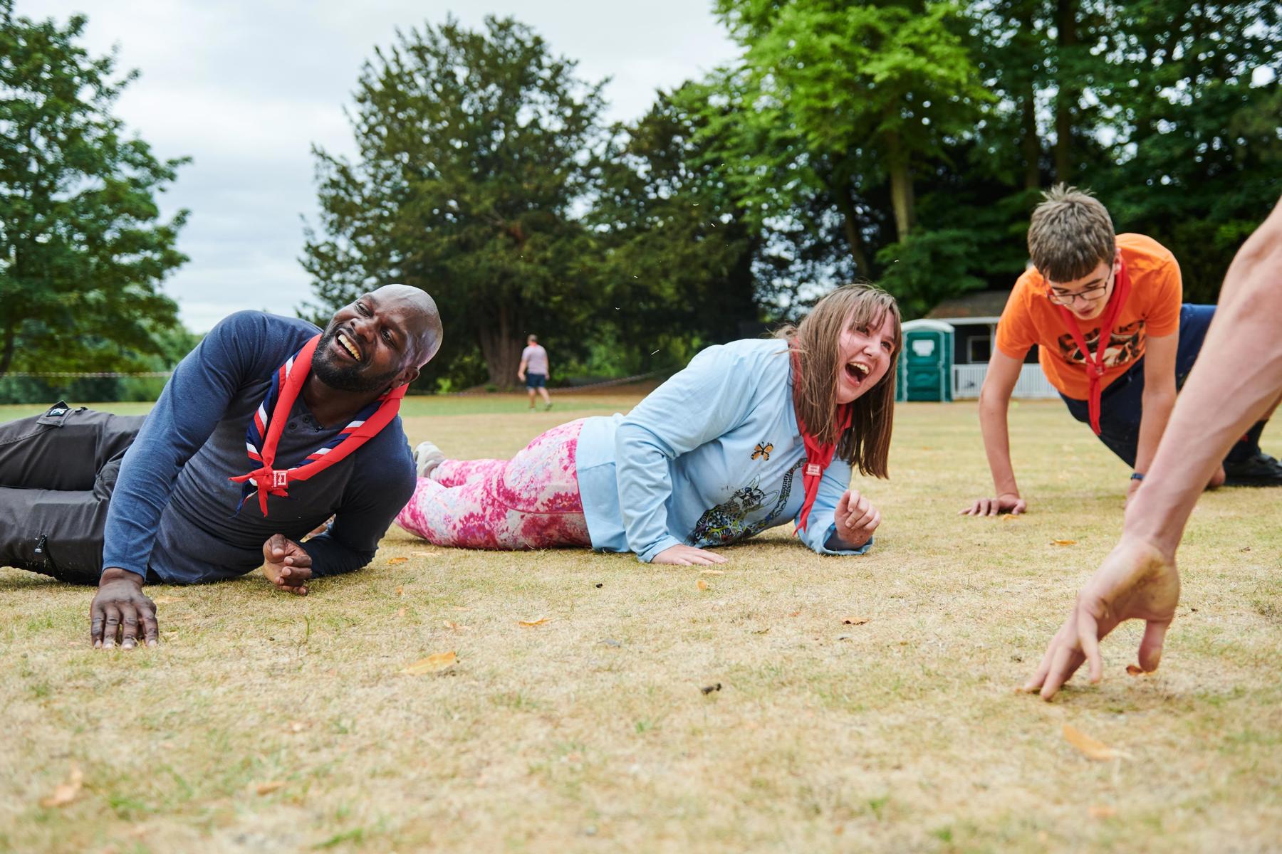Dwayne Fields is lying on the grass with Scouts laughing during an activity.