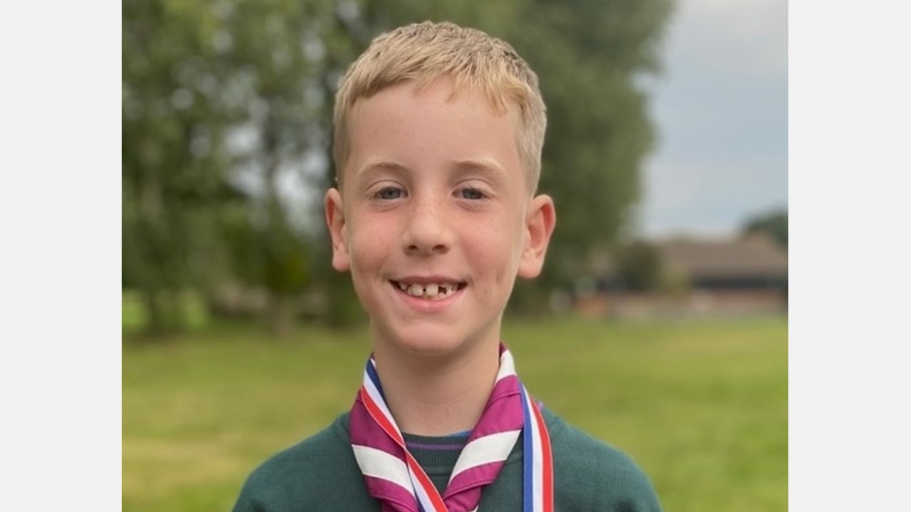 Cub Scout Luke smiles at the camera while wearing a green top and maroon and white necker.