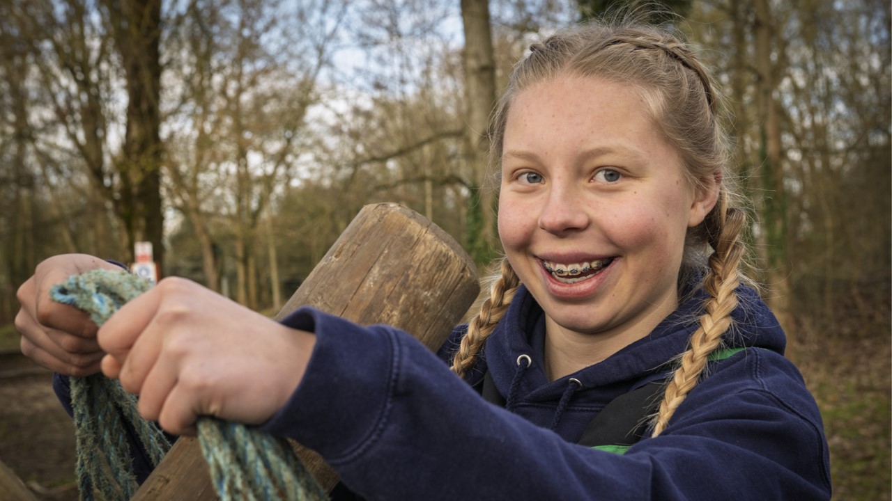 A young girl with braces smiles at the camera while holding onto a rope.