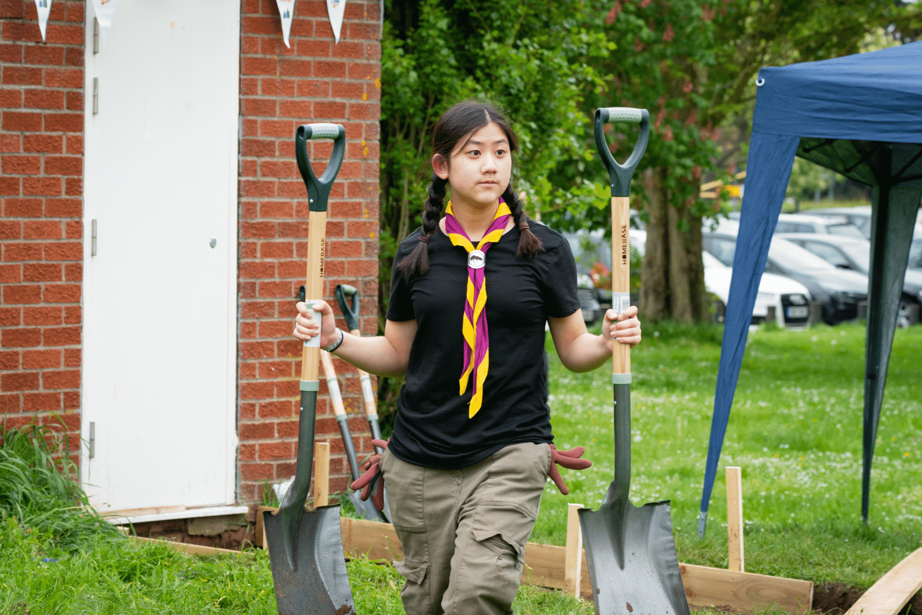 A Scout carrying spades at a local community project