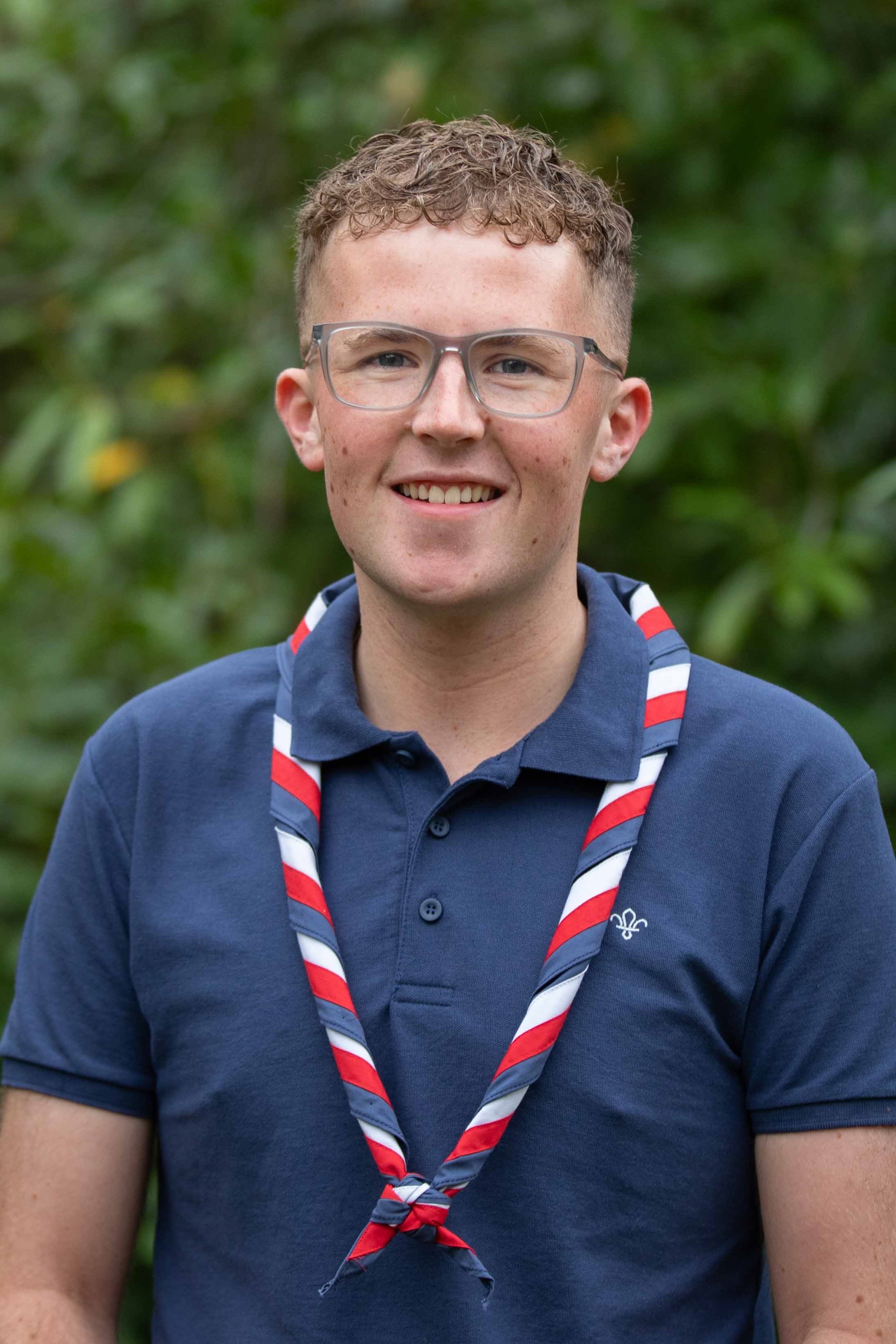 Olly, wearing a navy polo and red, white and blue necker, smiles at the camera.