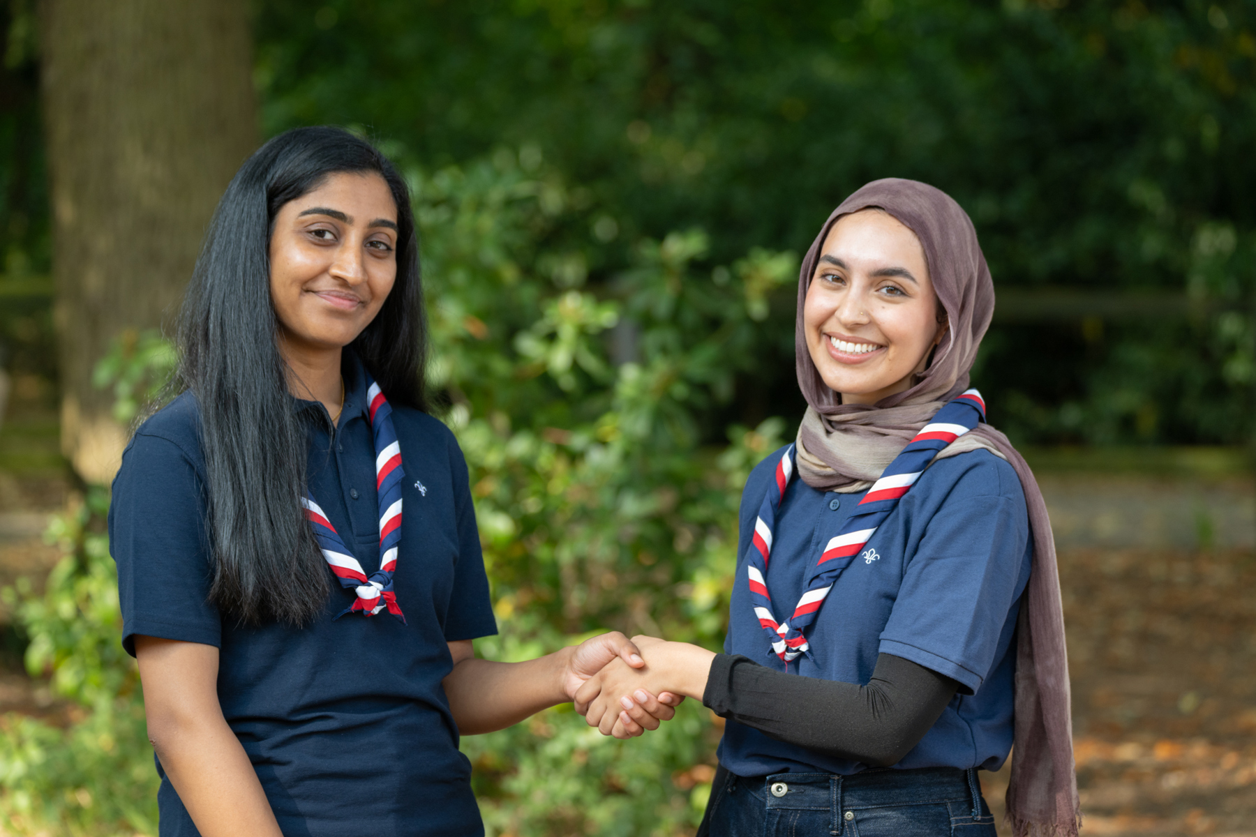 Two women wearing navy polos and UK neckers shaking hands