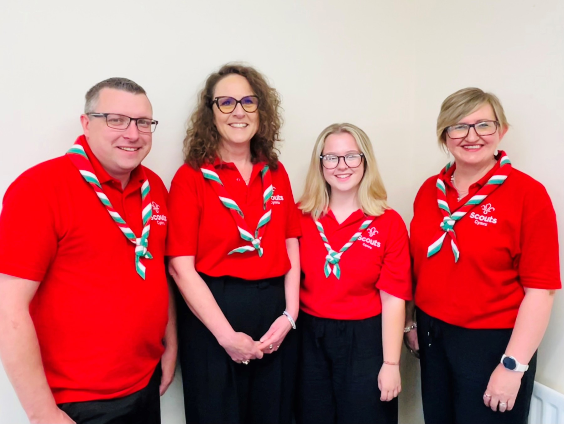 Three women and one man standing side by side in red polos