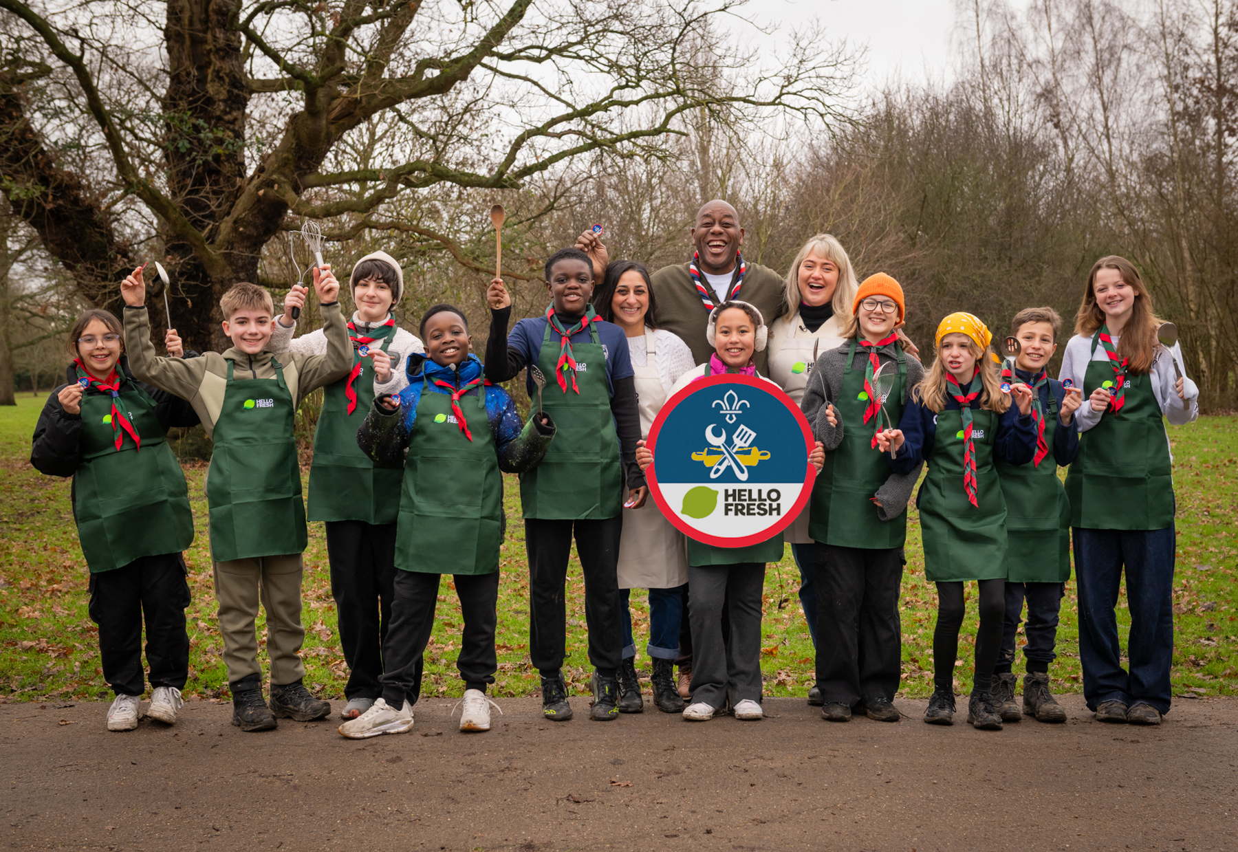 Ainsley Harriott stands with a big group of Scouts smiling at the camera, while one holds up a large Chef Badge.