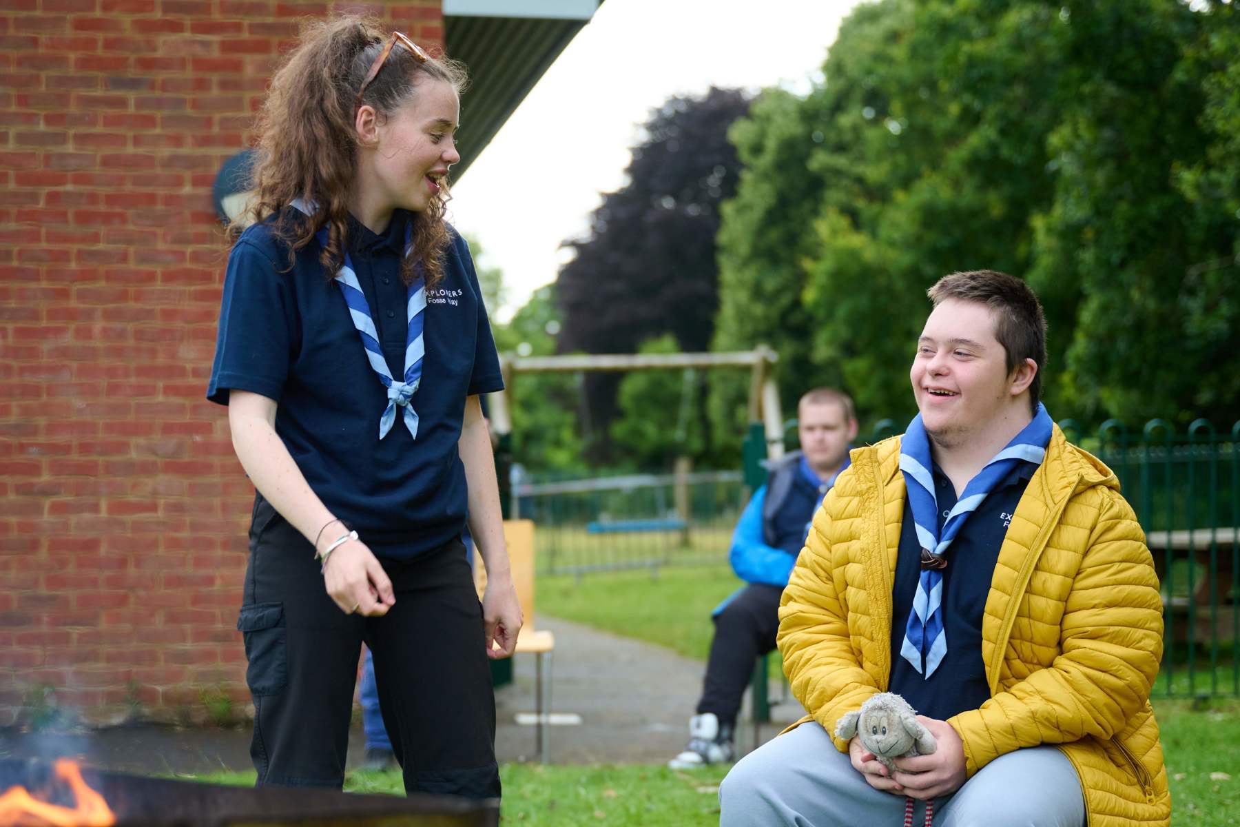 Two young people smile at each other while around a campfire.