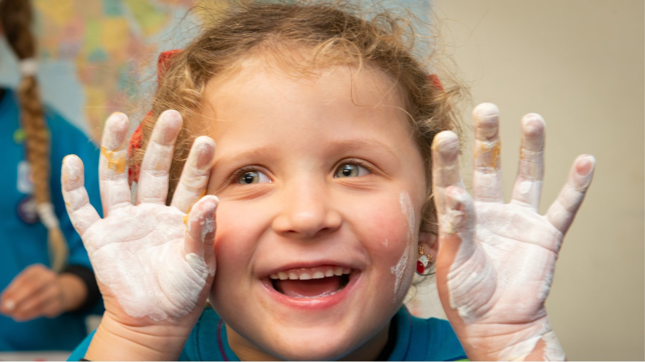A Beaver holds their hands, covered in white paint, up to their face while smiling.