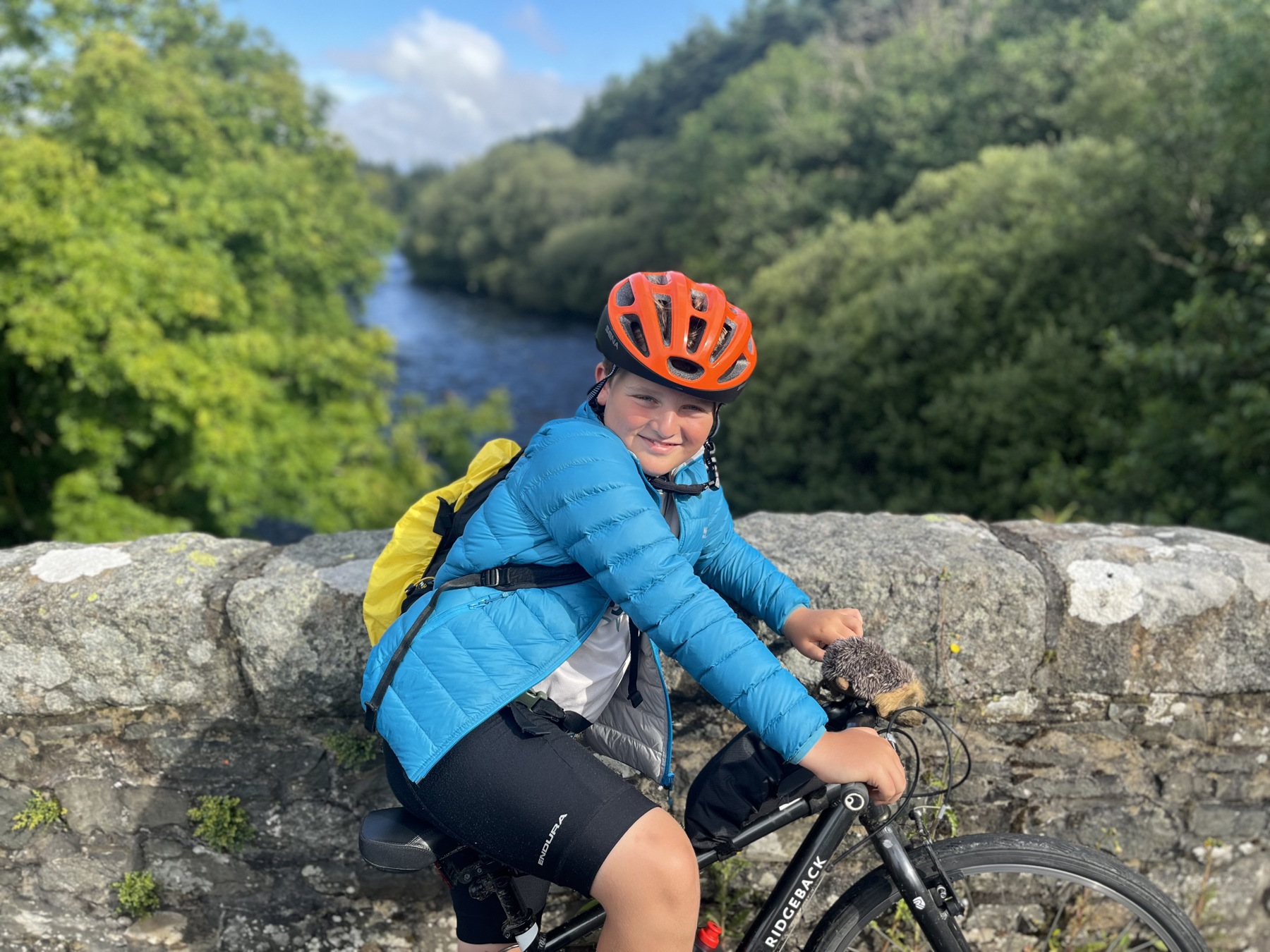 Harry on his bike on a stone bridge overlooking a river. He's wearing a red helmet.