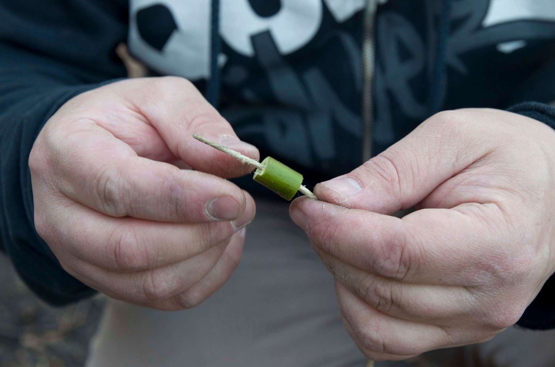 Hands threading a hollow piece of wood onto string.