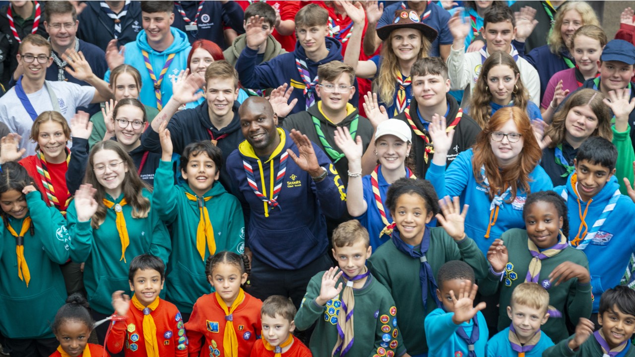 Dwayne Fields stands in the middle of a large group of young people, while they all wave at the camera.