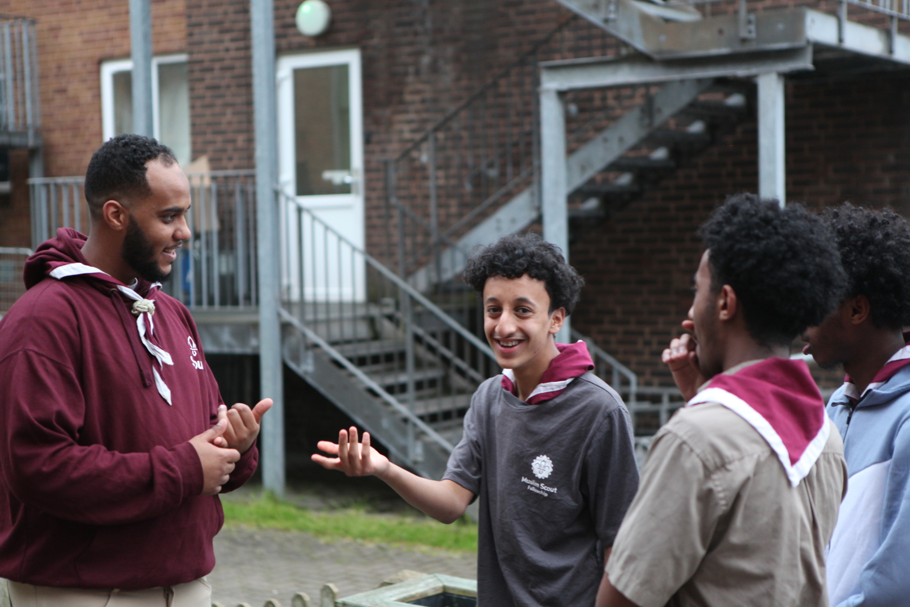 A Scout volunteer talking to three Scouts outside the building