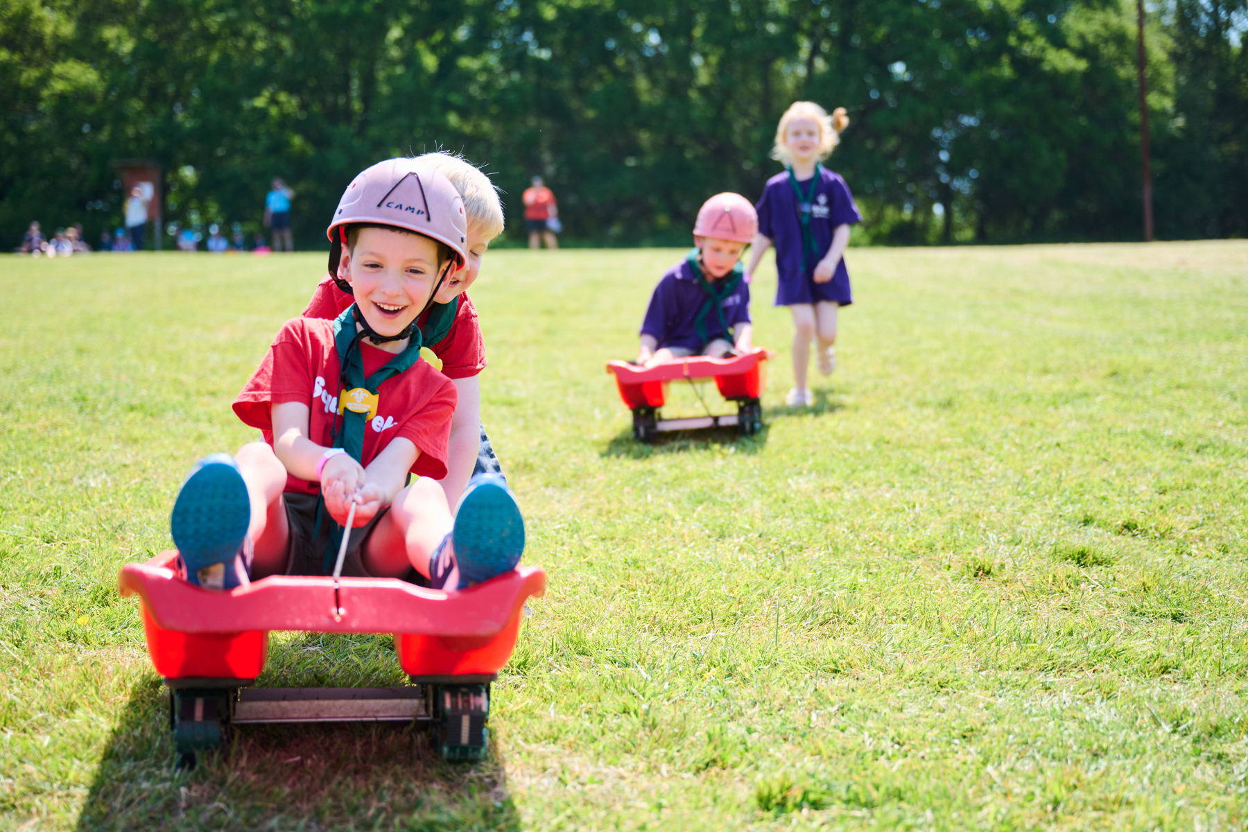 Two Squirrel Scouts using grass sledges, rolling down a field and wearing helmets