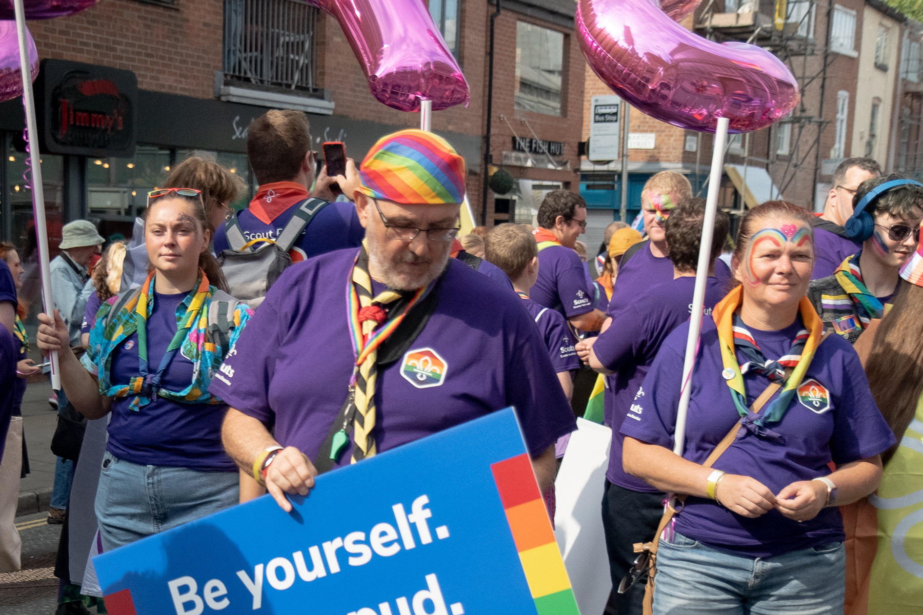 A group of Scouts waiting for a Pride parade to start with facepaint, balloons and banners