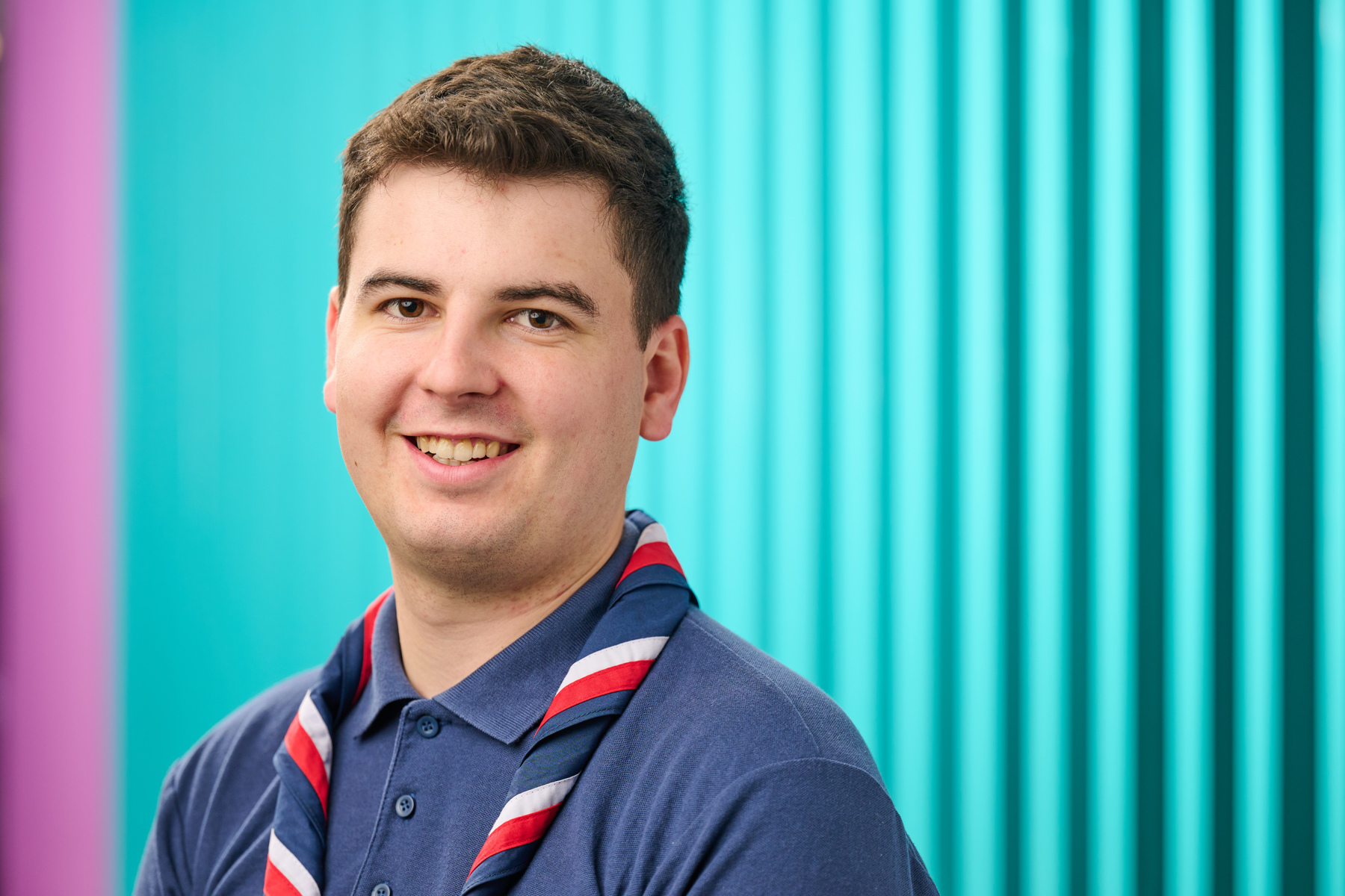 Callum Jones smiling and wearing a blue Scouts polo and red, white and blue necker.